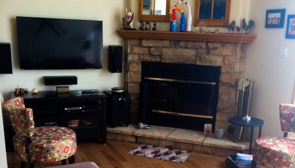 living room with hardwood floors, wood burning stone fireplace, flat screen tv and wall mounted sound system